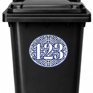 May include: A black trash bin with a white and blue oval sticker. The sticker features the numbers "123" in white, surrounded by a blue and white floral design.