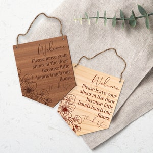 May include: Two wooden signs with a rope hanger, each with the text "Welcome Please leave your shoes at the door because little hands touch our floors Thank You" and a floral design.