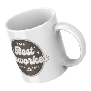 以下が含まれることがあります： 「The Best Coworker Gave Me This Mug」と書かれた茶色の円形デザインが施された白いセラミックマグカップです。