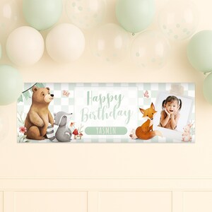 May include: A rectangular banner with a light green and white checkered background, featuring the text "Happy Birthday YASMIN". The banner includes illustrations of a bear, raccoon, fox, and a photo of a child. Balloons in shades of white and green are in the background.