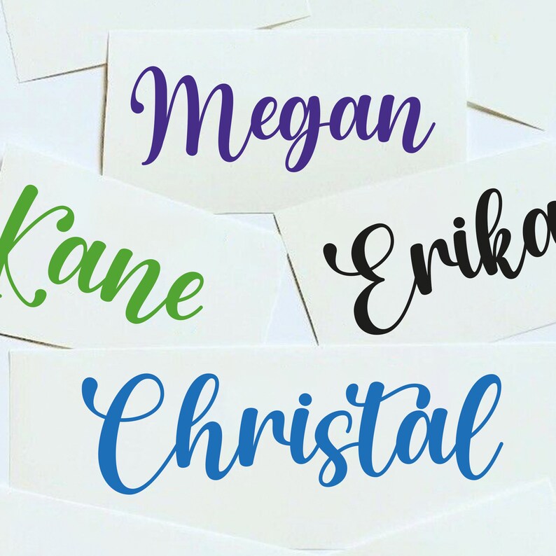 May include: Four white cards with names written in cursive on them. The names are Megan in purple, Kane in green, Erika in black, and Christal in blue.