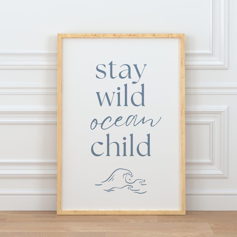 K&ouml;nnte beinhalten: Ein gerahmter Druck mit dem Text "stay wild ocean child" in blauer Schrift. Unter dem Text befindet sich eine stilisierte Wellengrafik.