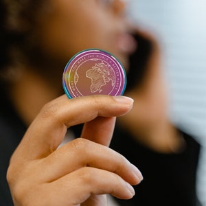 May include: A rainbow iridescent coin with the text "You make the world a better place from the" and a drawing of the world with Africa highlighted.