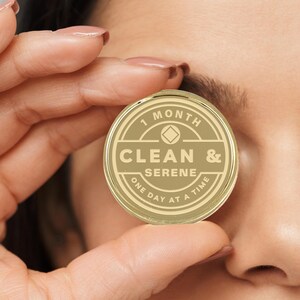 May include: Gold-colored round token with the text "1 Month Clean & Serene One Day At A Time" and a diamond symbol.