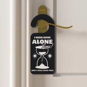 May include: Black door hanger with white text that reads "I need some alone time!" with an hourglass graphic and the text "(But I still love you)".