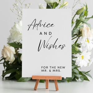 May include: White card with black calligraphy that reads "Advice and Wishes for the New Mr. & Mrs.". The card is on a small wooden easel.