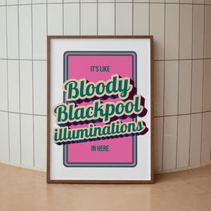 以下が含まれることがあります： 「IT'S LIKE Bloody Blackpool illuminations IN HERE」のテキストがレトロなスタイルで描かれたフレーム付きアートプリント。テキストはティールと白で、紫色の影があり、緑の縁取りのあるピンク色の背景に配置されています。