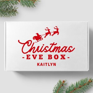 May include: White gift box with a red Christmas Eve Box design. The design features a red Santa Claus in a sleigh pulled by two reindeer. The text "Christmas - EVE BOX - Kaitlyn" is printed in red.