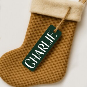 May include: A Christmas stocking with a waffle knit texture in a warm brown color. The top cuff is a cream-colored felt material. A green tag with the name "CHARLIE" in white lettering is attached with twine.