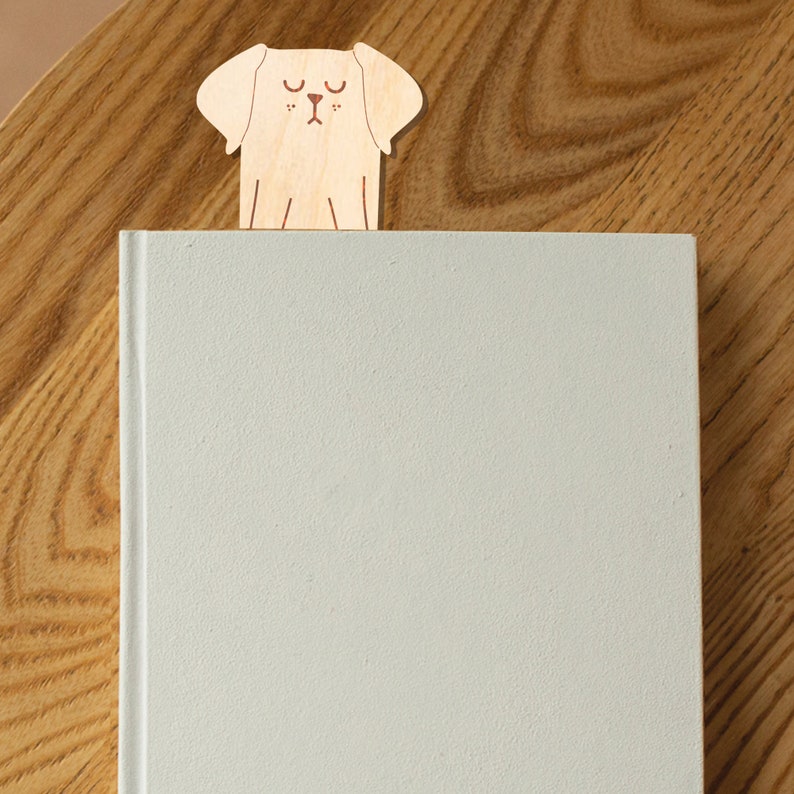 May include: A wooden bookmark shaped like a dog with closed eyes. The bookmark is light brown and has a white background.
