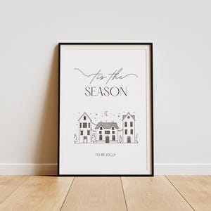 May include: Black and white printable art print with the text "Tis the season to be jolly" and a simple illustration of three houses with a crescent moon and stars in the sky.