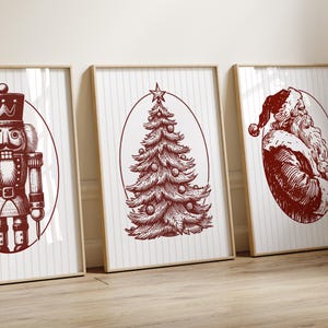 May include: Three framed Christmas-themed prints. The prints feature a nutcracker, a Christmas tree, and Santa Claus, all in a vintage red and white color scheme. The artwork is set against a striped background.