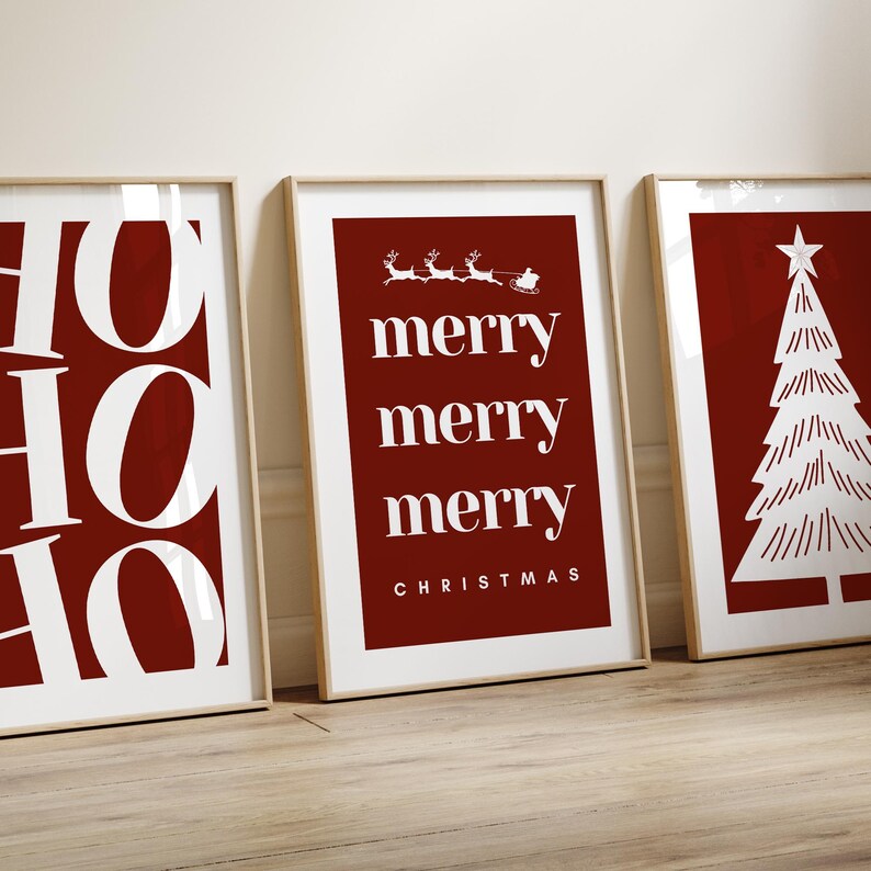 May include: Three framed Christmas art prints. The prints feature a red background with white text and images. One print says "HO HO HO", another says "merry merry merry CHRISTMAS", and the third shows a Christmas tree.