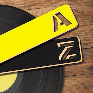 May include: Two wooden signs with the letters "A" and "Z" cut out. The "A" sign is yellow and the "Z" sign is black. The signs are placed on top of a black vinyl record.