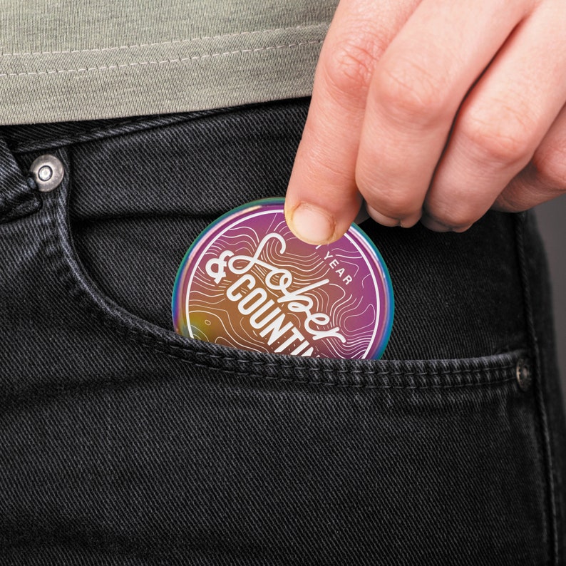 May include: A rainbow iridescent round sticker with the text "Year & counting" in white lettering. The sticker is in a person's back pocket.