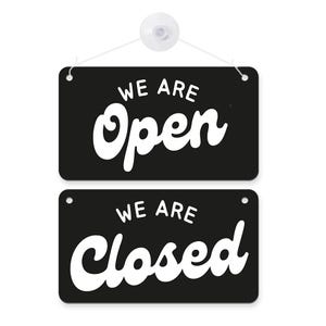 May include: Black rectangular sign with the words "WE ARE Open" in white, above a second sign with "WE ARE Closed" in white. The signs are hanging from a white string attached to a suction cup.