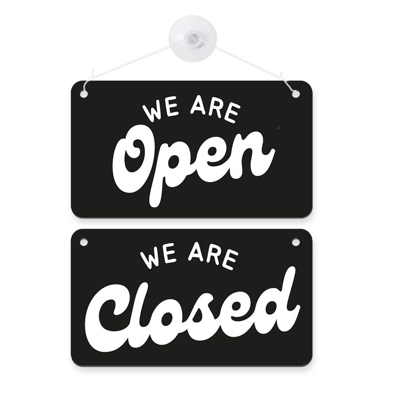 May include: Black rectangular sign with the words "WE ARE Open" in white, above a second sign with "WE ARE Closed" in white. The signs are hanging from a white string attached to a suction cup.