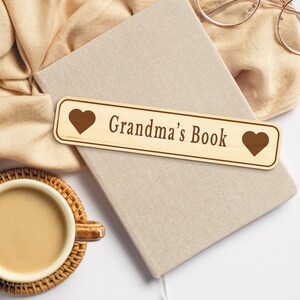 Op de afbeelding: Een houten bladwijzer met een hart aan elk uiteinde en de tekst "Grandma's Book" in bruine letters.