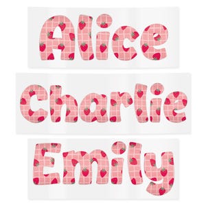 May include: Three rectangular stickers with names: "Alice", "Charlie", and "Emily". Each name is in a bubble letter font, filled with a strawberry pattern on a pink and white checkered background. The strawberries are red with green leaves.