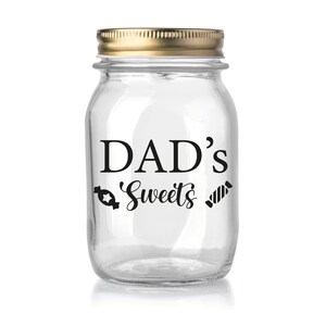 May include: A clear glass jar with a gold lid. The jar has a black vinyl sticker that says "DAD'S Sweets" with a candy cane and a ribbon on either side of the text.