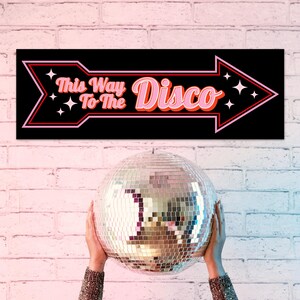 Pu&ograve; includere: Un cartello nero a forma di freccia con la scritta "This Way To The Disco" in rosa e arancione, e una palla da discoteca. Il cartello ha un contorno rosa e rosso con accenti di stelle bianche. La palla da discoteca &egrave; argentata e riflettente.