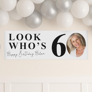 May include: A white banner with the text "LOOK WHO'S 60 Happy Birthday Helen" in black. A photo of a smiling woman is on the right. White and silver balloons are in the background.