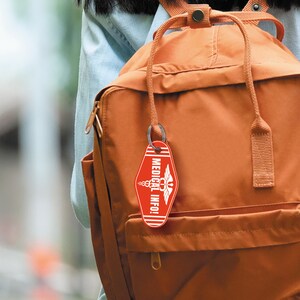 Puede incluir: Un llavero rojo con un s&iacute;mbolo m&eacute;dico blanco y el texto "MEDICAL INFO!" colgando de una mochila marr&oacute;n.
