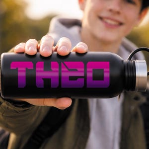 May include: Black water bottle with the name "THEO" in a purple and pink gradient font. The bottle has a black handle and a silver cap. The image is taken outdoors.