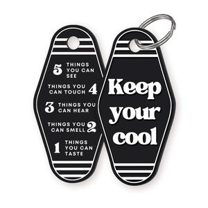 K&ouml;nnte beinhalten: Schwarz-wei&szlig;er Motel-Schl&uuml;sselanh&auml;nger mit dem Text "Keep your cool" auf der einen Seite und einer Liste von Dingen, die man sehen, ber&uuml;hren, h&ouml;ren, riechen und schmecken kann, auf der anderen Seite.