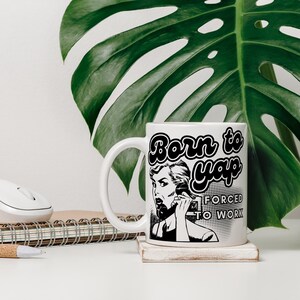 May include: White ceramic mug with a black and white illustration of a woman on the phone. The text "Born to yap forced to work" is printed on the mug.