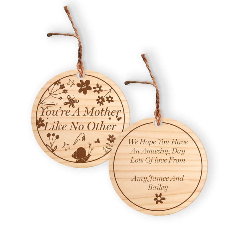 May include: Two round wooden ornaments with a brown twine string. The first ornament has a floral design with a butterfly and snail and the text "You're A Mother Like No Other". The second ornament has the text "We Hope You Have An Amazing Day Lots Of love From Amy, Jamee And Bailey" with a small flower at the bottom.