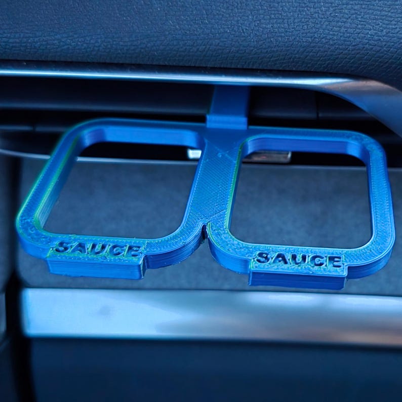 May include: A blue 3D printed car accessory with two cup holders. The holders are labeled "SAUCE" and are designed to fit in a car's air vent.