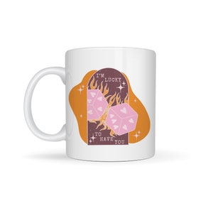 May include: White ceramic mug with a graphic of two pink dice with hearts on them, engulfed in flames. The text "I'm Lucky to Have You" is printed on the mug.