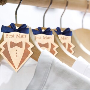 May include: Three wooden hangers with blue ribbon bows and tags that say "Best Man" with a tuxedo graphic.