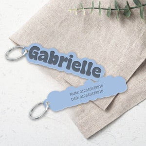 May include: A light blue personalized keychain with the name "Gabrielle" in black bubble letters. The keychain also has a space for phone numbers with the text "MUM: 012345678910 DAD: 012345678910".