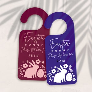 May include: Two Easter bunny door hangers, one burgundy with a pink bunny and the other blue with a white bunny. Both have the text "Easter Bunny" and "Please stop here for [name]" with the name Jess on the burgundy hanger and Sam on the blue hanger.