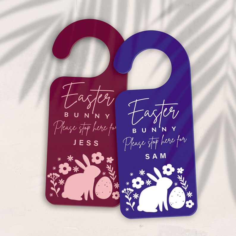 May include: Two Easter bunny door hangers, one burgundy with a pink bunny and the other blue with a white bunny. Both have the text "Easter Bunny" and "Please stop here for [name]" with the name Jess on the burgundy hanger and Sam on the blue hanger.