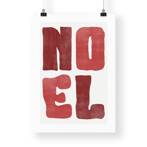 May include: A white poster featuring the word "NOEL" in large, red, block letters. The letters have a textured appearance. The poster is suspended by two black clips.