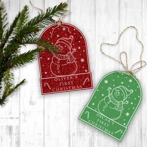 May include: Two red and green glitter Christmas ornaments with a snowman design and the text "Oliver's First Christmas" and "Oscar's First Christmas".