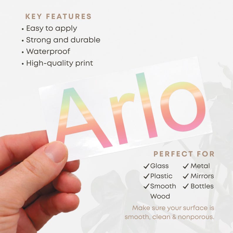 May include: A white sticker with the name "Arlo" in a gradient of colors from light green to pink. The sticker is held by a hand and is designed for glass, metal, plastic, mirrors, smooth wood, and bottles.
