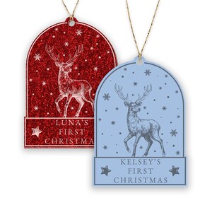 May include: Two Christmas ornaments featuring a deer in a snow globe design. The ornament on the left is red with glitter and says "Luna's First Christmas". The ornament on the right is blue and says "Kelsey's First Christmas".