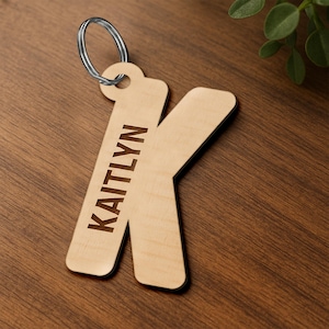 May include: Wooden keyring featuring the letter K and the name Kaitlyn engraved on it. The keyring is attached to a silver key ring.
