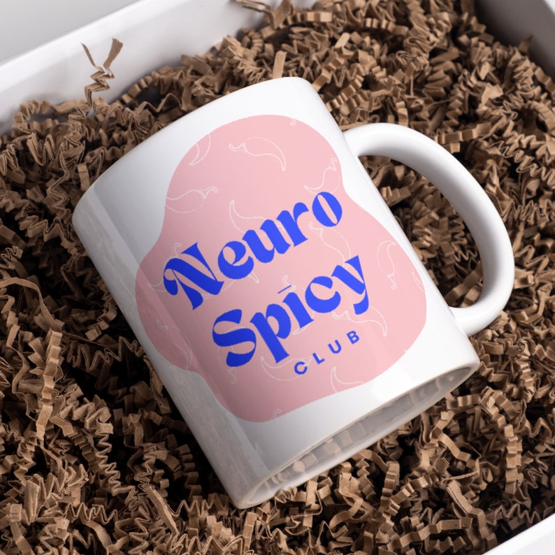 May include: White ceramic mug with a pink design and the text "Neuro Spicy Club" in blue lettering.