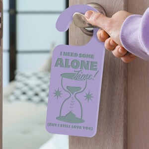 May include: Purple door hanger with the text "I need some alone time!" and an hourglass graphic. The text "(But I still love you)" is printed below the hourglass.