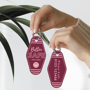 May include: Two burgundy motel keychains with pink stripes. One keychain says "Better Safe Than Sorry" with a pink smiley face. The other keychain says "Please Call: 0123 123456".