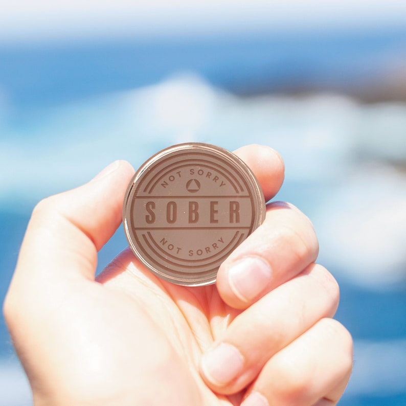 May include: A round, brown token with the words "Not Sorry" and "Sober" on it. The token has a triangle symbol in the center.