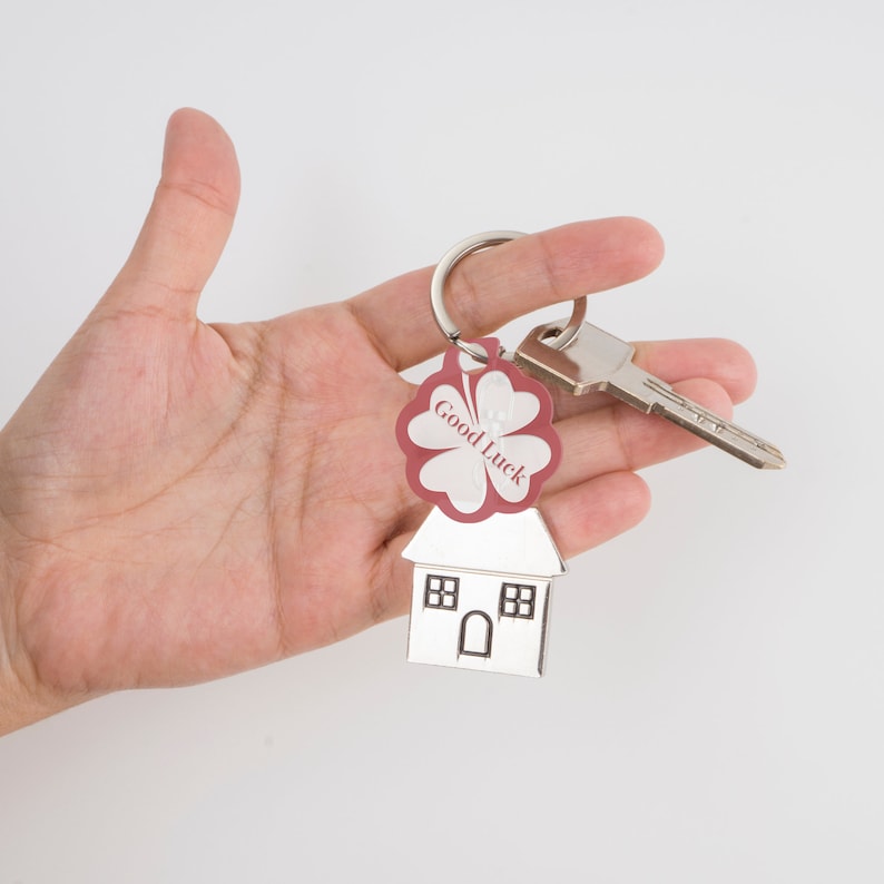May include: A silver house-shaped keyring with a red four-leaf clover charm that says "Good Luck".