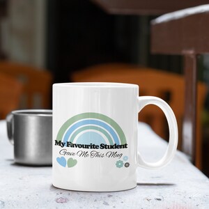 May include: White ceramic mug with a rainbow design and the text "My Favourite Student Gave Me This Mug".