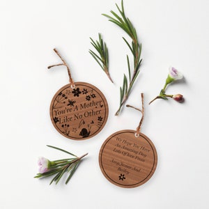 May include: Two round wooden ornaments with engraved text. The first ornament has a floral design and the text "You're a Mother Like No Other". The second ornament has the text "We Hope You Have An Amazing Day Lots of Love From Amy, Jamee and Bailey".
