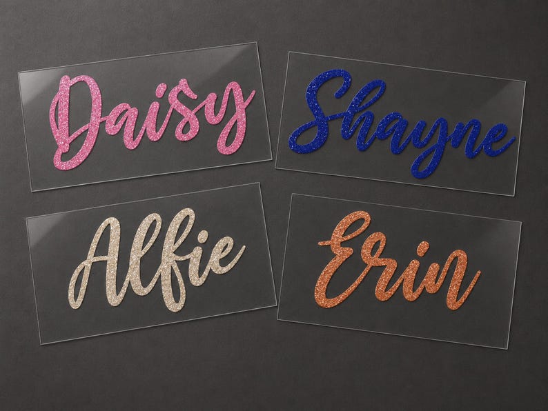 May include: Four clear acrylic name tags with glitter lettering. The names are Daisy in pink, Shayne in blue, Alfie in beige, and Erin in orange. The names are in a cursive font, and the background is dark gray.